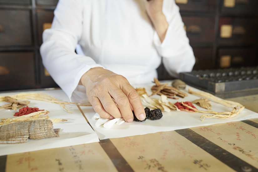 Close-up image of Chinese pharmacy worker choosing dry berries and mushrooms for customer