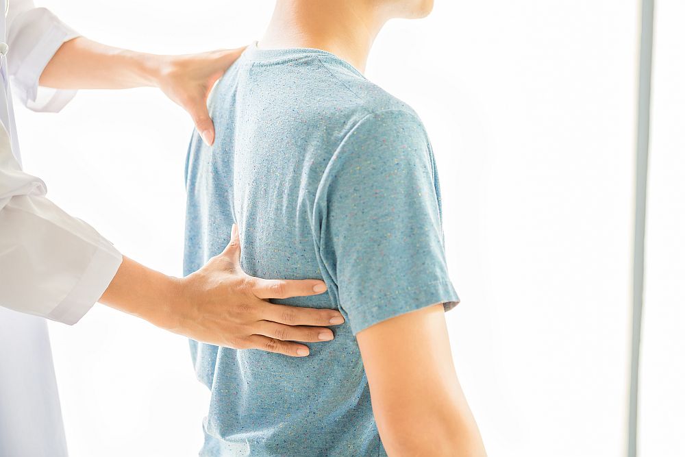 A person in a blue shirt receives chiropractic treatment as a healthcare professional places hands on the person's upper back.
