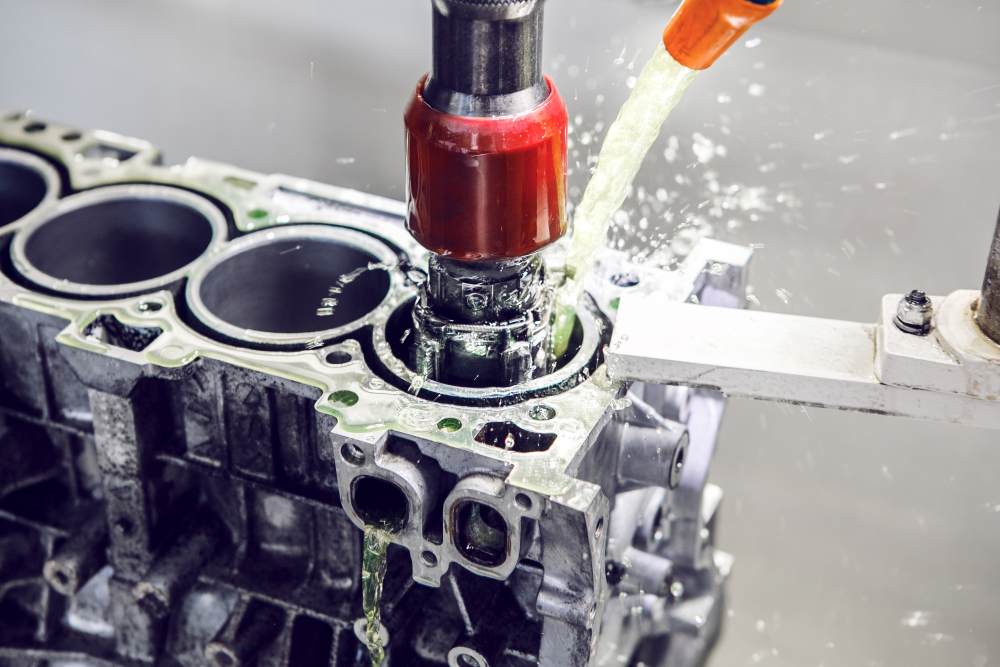 A machine tool drills into an engine block while coolant fluid is sprayed onto the cutting area to reduce heat and friction, demonstrating advanced techniques similar to Metal Injection Molding Services for complex and precision components.